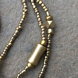 K&ouml;nnte beinhalten: Eine goldene Perlenkette mit einer zylindrischen und einer sechseckigen Perle. Die Kette besteht aus kleinen, runden Perlen.