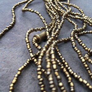 K&ouml;nnte beinhalten: Nahaufnahme einer goldenen Perlenkette mit mehreren Str&auml;ngen. Die Kette besteht aus kleinen, runden Perlen und hat ein schlichtes, elegantes Design.