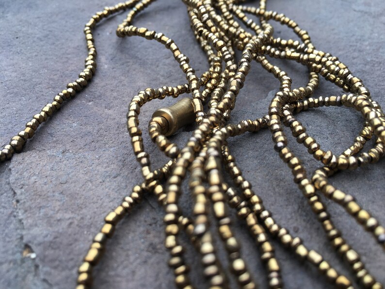 K&ouml;nnte beinhalten: Nahaufnahme einer goldenen Perlenkette mit mehreren Str&auml;ngen. Die Kette besteht aus kleinen, runden Perlen und hat ein schlichtes, elegantes Design.