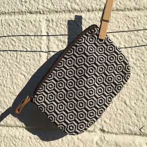 Puede incluir: Una pequeña bolsa con cremallera de patrón geométrico blanco y negro colgando de una cuerda para tender la ropa con una pinza de madera.