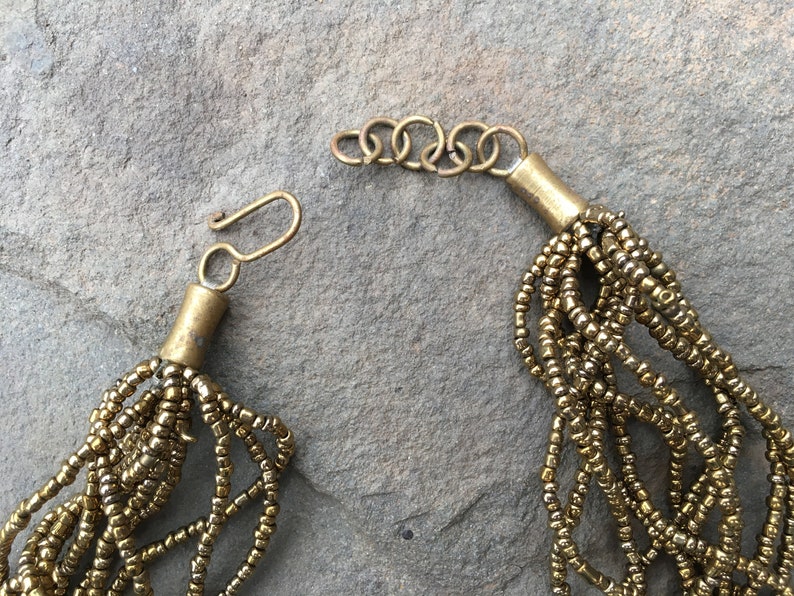 K&ouml;nnte beinhalten: Eine goldene Perlenkette mit einem Karabinerverschluss. Die Kette besteht aus mehreren Str&auml;ngen kleiner, runder Perlen.