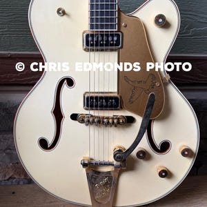 May include: Cream-colored electric guitar with gold hardware and a decorative pickguard featuring a bird design. The guitar has a classic body shape, f-holes, and the text "© CHRIS EDMONDS PHOTO".