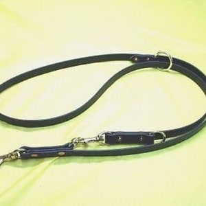 May include: A black leather dog lead with two metal clips and a metal ring. The lead is designed for walking two dogs.