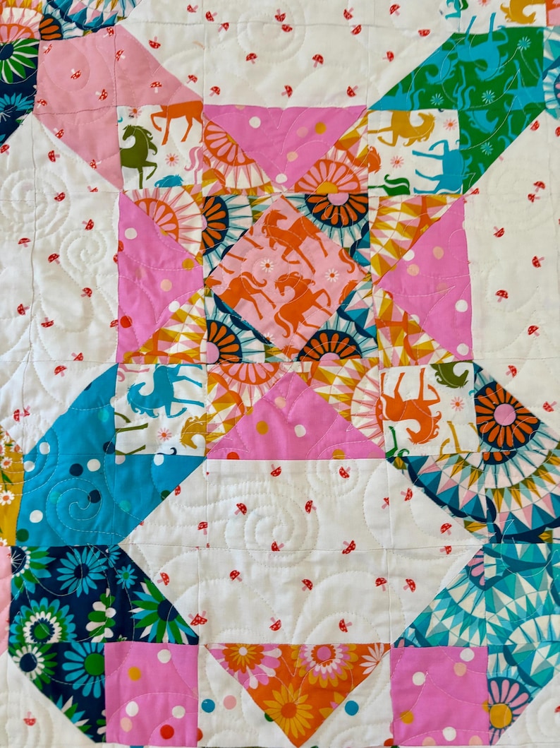 Puede incluir: Una colcha de patchwork con un patr&oacute;n geom&eacute;trico repetitivo de cuadrados y tri&aacute;ngulos. La tela muestra una variedad de estampados coloridos que incluyen caballos estilizados, motivos florales de sol y peque&ntilde;os hongos rojos sobre un fondo blanco.