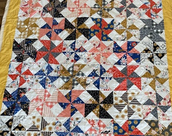 Puede incluir: Una colcha blanca con un borde amarillo. La colcha está hecha de un mosaico de diferentes telas con patrones florales, geométricos y de lunares en tonos de rojo, azul, negro, blanco y dorado.