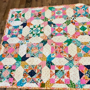 May include: A patchwork quilt featuring a repeating block pattern with a variety of colorful floral, geometric, and animal-print fabrics in shades of pink, teal, orange, and yellow, interspersed with cream-colored fabric squares with small red dots.