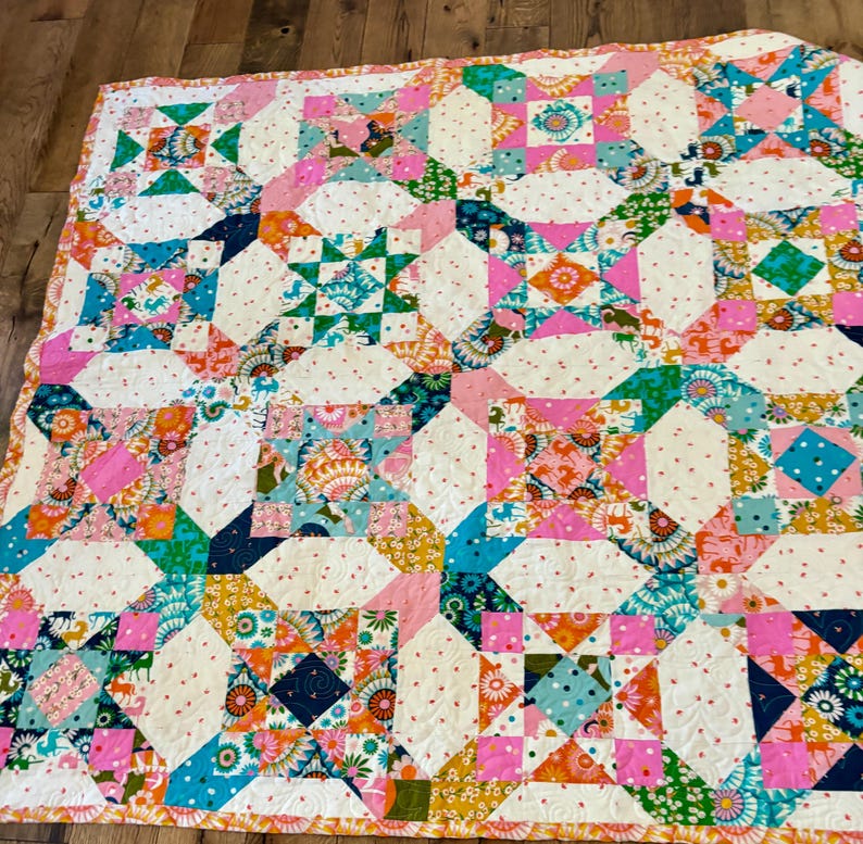 Puede incluir: Una colcha de patchwork con un patr&oacute;n de bloques repetitivos que presenta una variedad de telas coloridas con estampados florales, geom&eacute;tricos y de animales en tonos rosa, turquesa, naranja y amarillo, intercaladas con cuadrados de tela crema con puntos rojos.