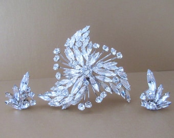 May include: A vintage rhinestone brooch and earrings set. The brooch features a large, sparkling cluster of clear rhinestones in a floral design. The earrings are smaller, matching clusters of rhinestones.