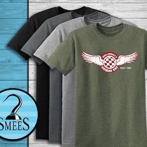 May include: A collection of short-sleeved t-shirts in various colors: black, charcoal, gray, and olive green. The olive green shirt features a distressed graphic with the text "Jock Lindsey's Hangar Bar ESTD 1955" and a wing design.