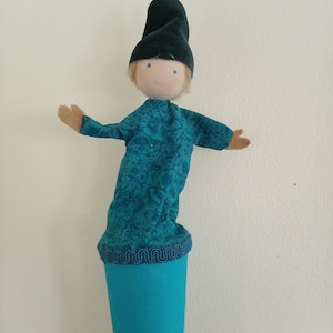 May include: A teal blue puppet with a green felt hat and a patterned teal blue shirt. The puppet is attached to a teal blue cone.