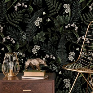 May include: Dark, moody wallpaper featuring a botanical design with ferns, flowers, and berries in shades of green and white against a black background. A gold wireframe lamp, a geometric bear statue, and a gold chair add a touch of elegance.