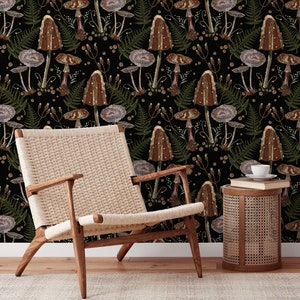 May include: A black and white wallpaper with an embroidered pattern of mushrooms and ferns. A light brown wicker side table with a book and a white cup on top sits in front of the wallpaper. A light brown wicker chair with a woven seat sits in front of the table.