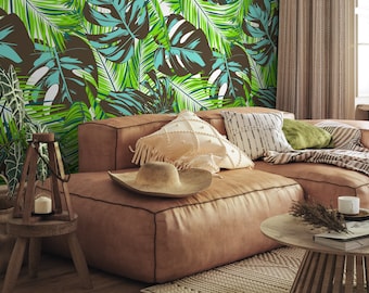 May include: A brown leather sofa with cushions and a straw hat, set against a wall with a tropical leaf wallpaper featuring green and brown leaves.