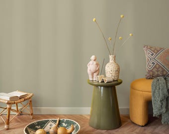 May include: A decorative interior scene featuring a green side table with a vase, a sculpture, and a candle. A woven bowl with gourds sits on the floor. A yellow ottoman and a patterned pillow are also visible.