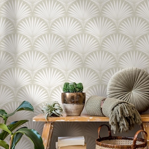 May include: A neutral-toned room with a wallpaper featuring a repeating white fan-like pattern. A wooden bench holds a potted cactus, a small plant, a woven blanket, and a round, tufted pillow. A wicker basket sits below.