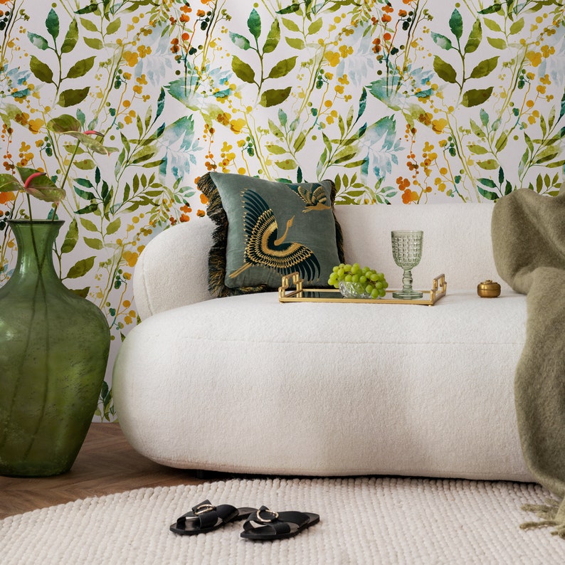 May include: A white couch with a green throw blanket and a green vase. The couch has a floral patterned wallpaper behind it. There is a tray with a glass of water and a bowl of grapes on the couch.