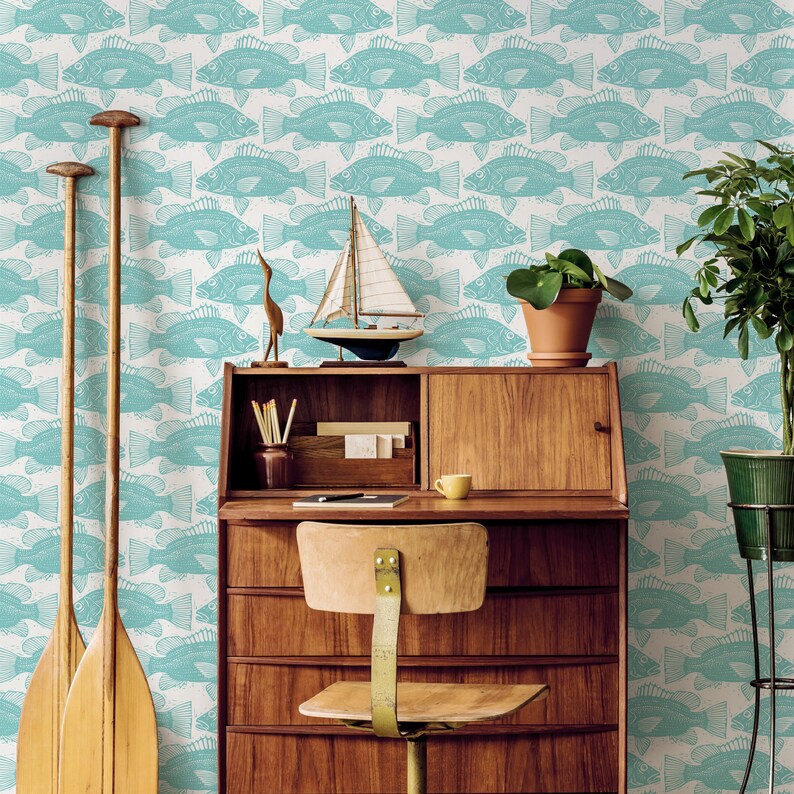 May include: A wooden desk with a light wood finish and a light blue wallpaper with a pattern of fish. The desk has a top drawer, a lower drawer, and a small shelf. There is a chair in front of the desk. There are two wooden paddles leaning against the wall.