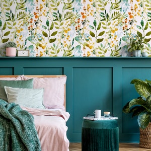 May include: A teal green headboard with a pink and white striped bedspread. A green throw blanket is draped over the bed. A small green velvet ottoman with a tray and a white mug sits in front of the bed. A large green plant is in a wicker basket on the right side of the image. The wall behind the bed is covered in a white wallpaper with a watercolor floral pattern in shades of green, yellow, and orange.