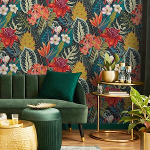 May include: A vibrant interior scene featuring a dark floral wallpaper with red, pink, and yellow flowers and green leaves. A green velvet sofa and ottoman are in the foreground, with gold accent tables and a potted plant. The overall theme is tropical and luxurious.