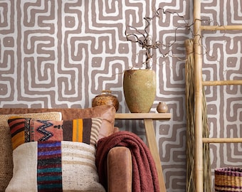 Può includere: Un salotto con un divano in pelle marrone adornato da cuscini fantasia colorati e una coperta bordeaux. Lo sfondo mostra una parete con un motivo a labirinto ripetuto in marrone e bianco. Sono visibili anche una scala di legno e un vaso decorativo.