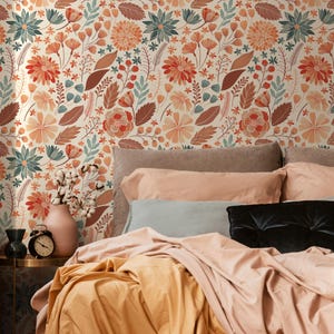 May include: A bedroom scene featuring a bed with peach and gold bedding, a gray headboard, and a floral wallpaper background. The wallpaper has a repeating pattern of orange, red, and teal flowers and leaves. A small table holds a pink vase, a black alarm clock, and two small black vases.