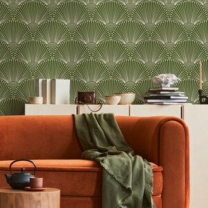 K&ouml;nnte beinhalten: Eine gr&uuml;n-wei&szlig;e geometrische Tapete mit einem braunen Samtsofa und einer gr&uuml;nen Wolldecke. Das Sofa steht vor einem wei&szlig;en Regal mit B&uuml;chern und Dekoartikeln.
