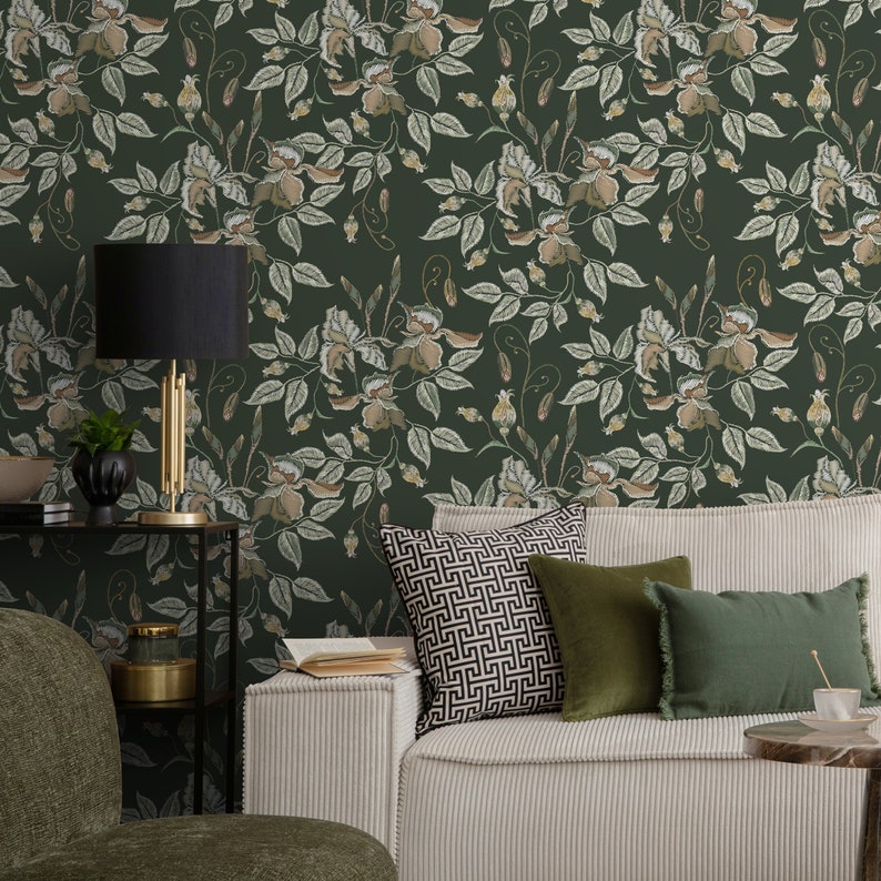 May include: A living room interior with a green floral wallpaper, a white couch with green and black patterned pillows, a black side table with a gold lamp, and a book on the couch.