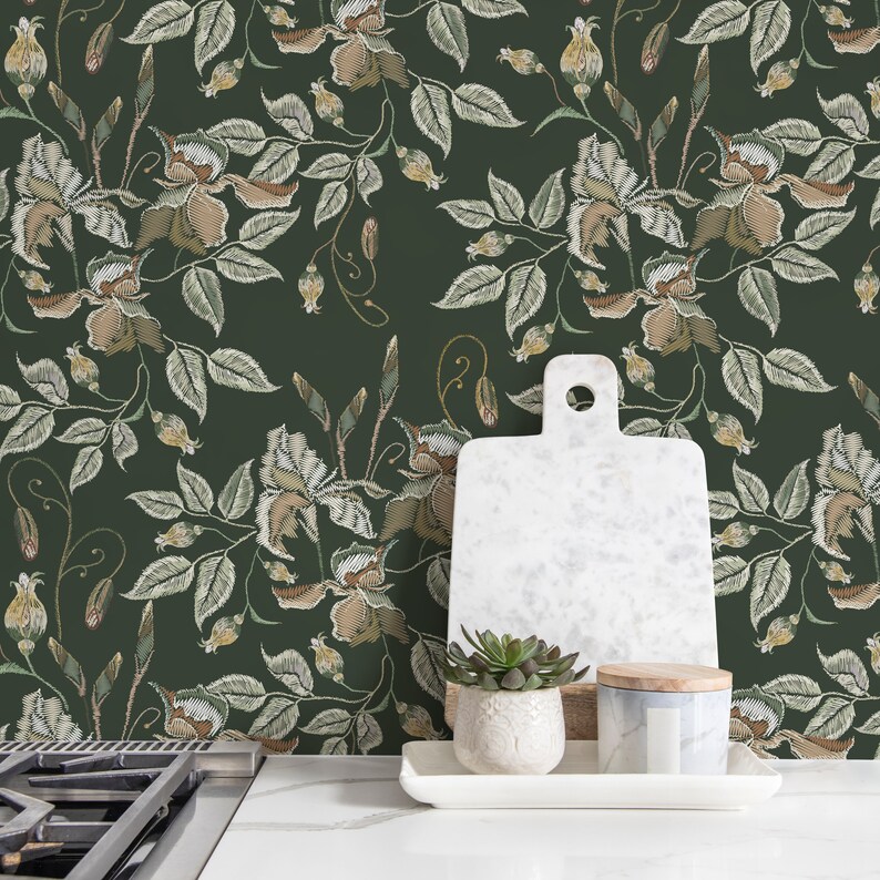 May include: A green wallpaper with an embroidered floral pattern. The wallpaper is displayed in a kitchen setting with a white cutting board, a small potted succulent, and a white ceramic jar with a wooden lid.