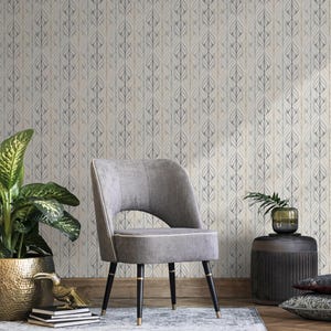 May include: A gray upholstered chair with a curved back and black legs with gold accents. The chair sits in front of a wallpaper with a repeating leaf pattern in shades of gray and beige. A potted plant and side table are also visible.