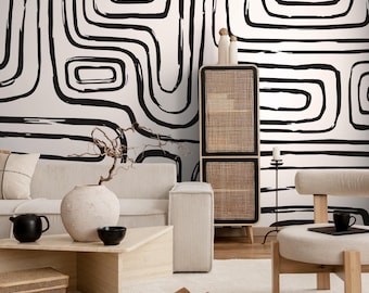 Può includere: Un moderno soggiorno con un motivo astratto in bianco e nero sulla parete. La stanza è dotata di un divano beige, un tavolino in legno, un mobiletto in tessuto e una sedia beige. Gli elementi decorativi includono un vaso, una teiera nera e una piccola ciotola nera.