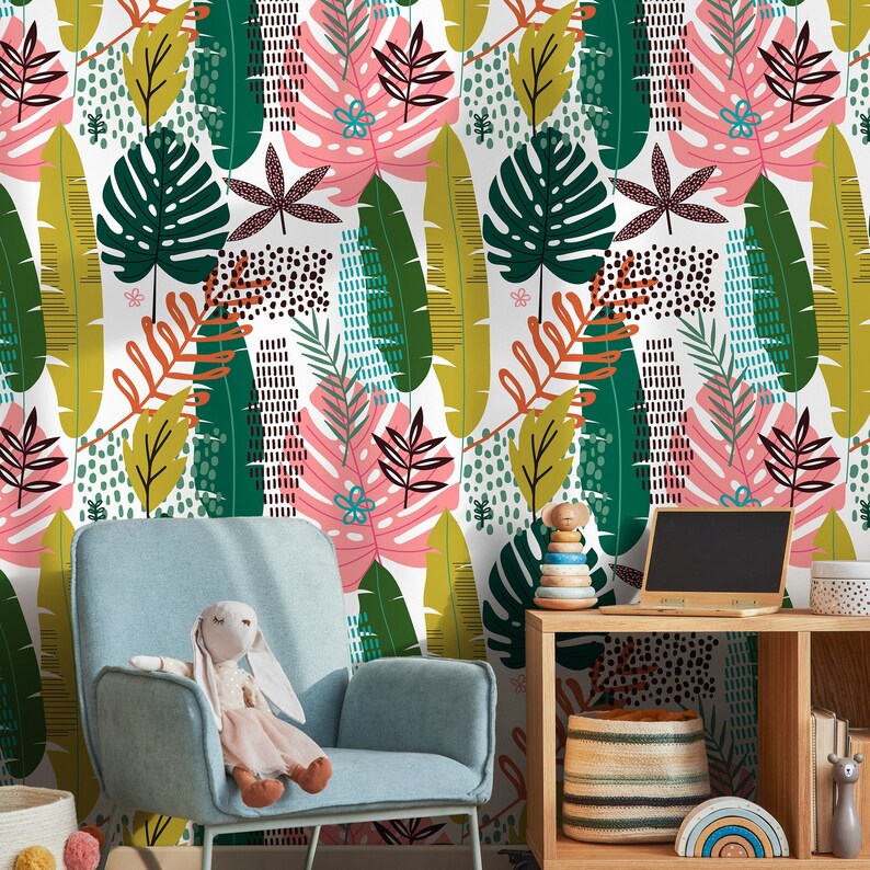 May include: A white background with a colorful tropical leaf pattern. The wallpaper features green, pink, yellow, and brown leaves and geometric shapes. A blue armchair with a stuffed animal sits in front of the wallpaper. A wooden shelf with a toy and a basket sits in the foreground.