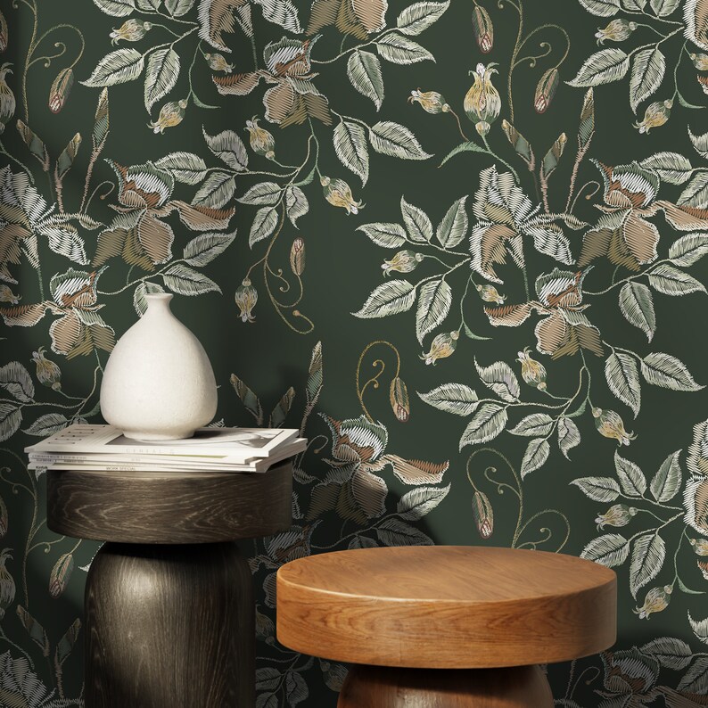 May include: A dark green wallpaper with a floral pattern. The pattern features white embroidered flowers and leaves. The wallpaper is displayed on a wall with two wooden stools in front of it.