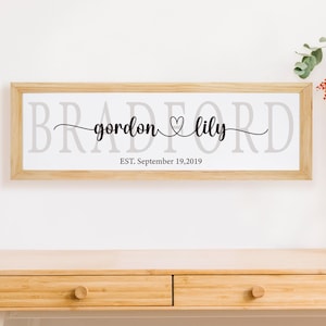 Puede incluir: Una impresión enmarcada con el texto "BRADFORD" en letras grandes, con los nombres "gordon" y "lily" escritos en cursiva con un símbolo de corazón entre ellos. El texto "EST. Septiembre 19, 2019" está debajo de los nombres.