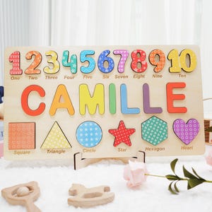 May include: A colorful wooden puzzle with numbers 1 through 10, the name "Camille" spelled out, and various shapes including a square, triangle, circle, star, hexagon, and heart. Each piece has a different pattern.