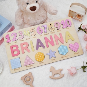 Op de afbeelding: Een houten puzzelbord met de naam BRIANNA in grote gekleurde letters, de cijfers &eacute;&eacute;n tot en met tien met bijbehorende labels, en diverse vormen zoals een vierkant, driehoek, cirkel, ster, zeshoek en hart met hun namen.