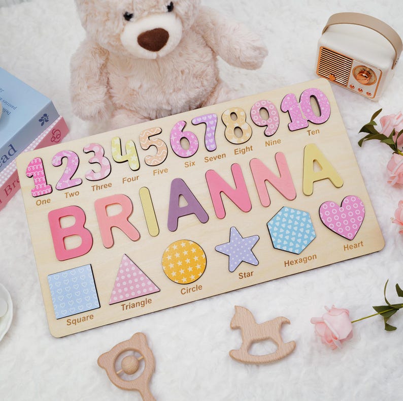 Op de afbeelding: Een houten puzzelbord met de naam BRIANNA in grote gekleurde letters, de cijfers &eacute;&eacute;n tot en met tien met bijbehorende labels, en diverse vormen zoals een vierkant, driehoek, cirkel, ster, zeshoek en hart met hun namen.