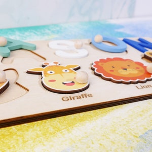 May include: Wooden puzzle with colorful animal illustrations and letters. The puzzle pieces include a giraffe, lion, and the letters A, O, N. The puzzle is made of light wood and has a natural finish.