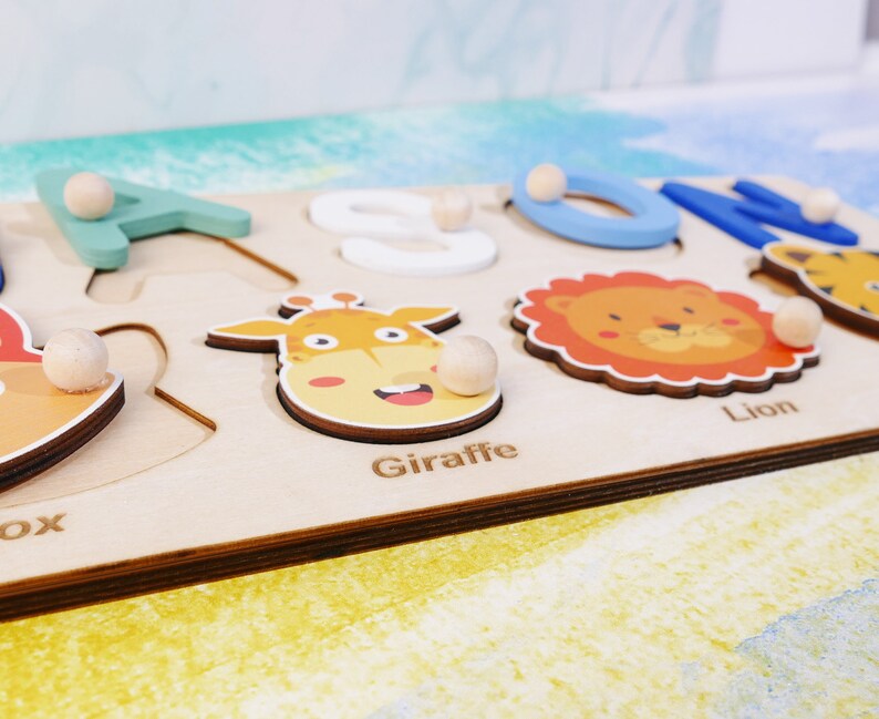 May include: Wooden puzzle with colorful animal illustrations and letters. The puzzle pieces include a giraffe, lion, and the letters A, O, N. The puzzle is made of light wood and has a natural finish.