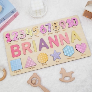 Op de afbeelding: Een rechthoekig houten puzzelbord met de naam BRIANNA in grote gekleurde letters, de cijfers &eacute;&eacute;n tot en met tien met bijbehorende labels, en diverse vormen zoals een vierkant, driehoek, cirkel, ster, zeshoek en hart.