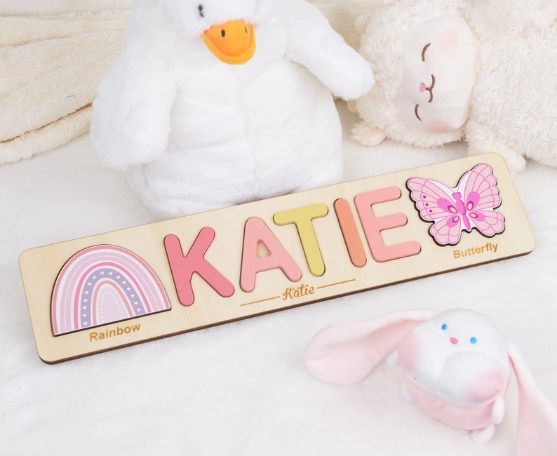 May include: Personalized wooden puzzle with the name "KATIE" spelled out in colorful letters. The puzzle also features a rainbow, a butterfly, and the words "Rainbow", "Butterfly", and "Katie".