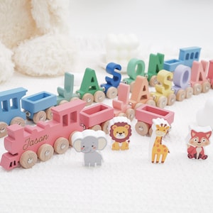 May include: A wooden toy train set featuring a pink engine with the name Jason engraved on the side. The train includes colorful letter-shaped carriages and separate wooden animal figures, including an elephant, a lion, a giraffe, and a fox.