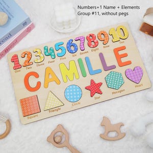 Op de afbeelding: Een houten puzzelbord met de naam CAMILLE in gekleurde letters, de cijfers &eacute;&eacute;n tot en met tien, en diverse vormen zoals een vierkant, driehoek, cirkel, ster, zeshoek en hart, elk gelabeld met de bijbehorende naam in het Engels.