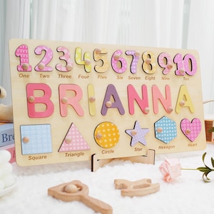 A wooden learning toy with colorful numbers 1 through 10, with a custom name  spelled out, and shapes including a square, triangle, circle, star, hexagon, and heart. Each piece has a different pattern and is designed to be removed and replaced.