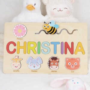 May include: A wooden personalised puzzle featuring the name Christina. The puzzle includes a bee, flower, giraffe, rabbit, horse and cat. This puzzle is a great educational toy for children.