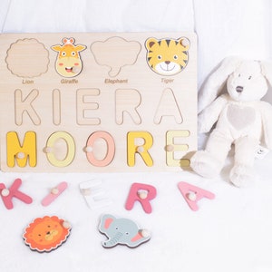 May include: A wooden personalized puzzle with the name KIERA MOORE. The puzzle features colorful letters and animal shapes, including a lion, giraffe, elephant, and tiger. The puzzle pieces are separate and can be placed in the corresponding cutouts on the board.