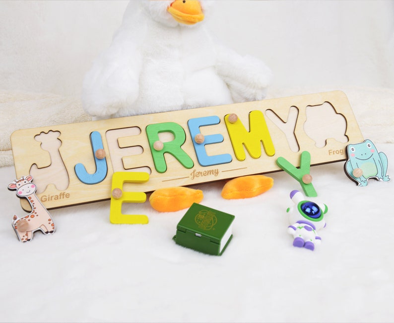 May include: A wooden personalized name puzzle with colorful letters spelling out the name "Jeremy". The puzzle includes a giraffe, frog, and a small toy robot.