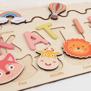 May include: Wooden puzzle with colourful animal and rainbow pieces. The puzzle is shaped like the name "Katie" and includes the words "Rainbow", "Fox", "Giraffe", and "Lion".
