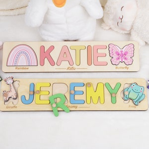 May include: Two wooden personalized name puzzles with colorful letters and animal illustrations. The top puzzle has a rainbow, butterfly, and the name "KATIE". The bottom puzzle has a giraffe, frog, and the name "JEREMY".