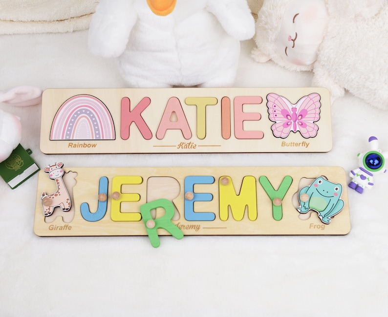 May include: Two wooden personalized name puzzles with colorful letters and animal illustrations. The top puzzle has a rainbow, butterfly, and the name "KATIE". The bottom puzzle has a giraffe, frog, and the name "JEREMY".