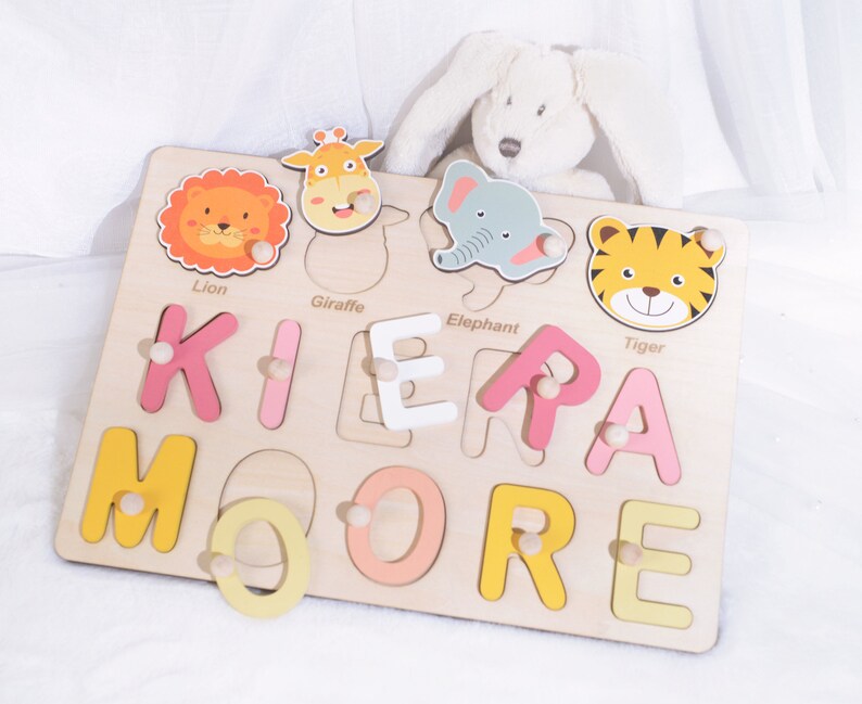 May include: Wooden puzzle with colorful animal and letter pieces. The puzzle is shaped like a rectangle and has a light wood finish. The letters spell out the name "KIERA MOORE".
